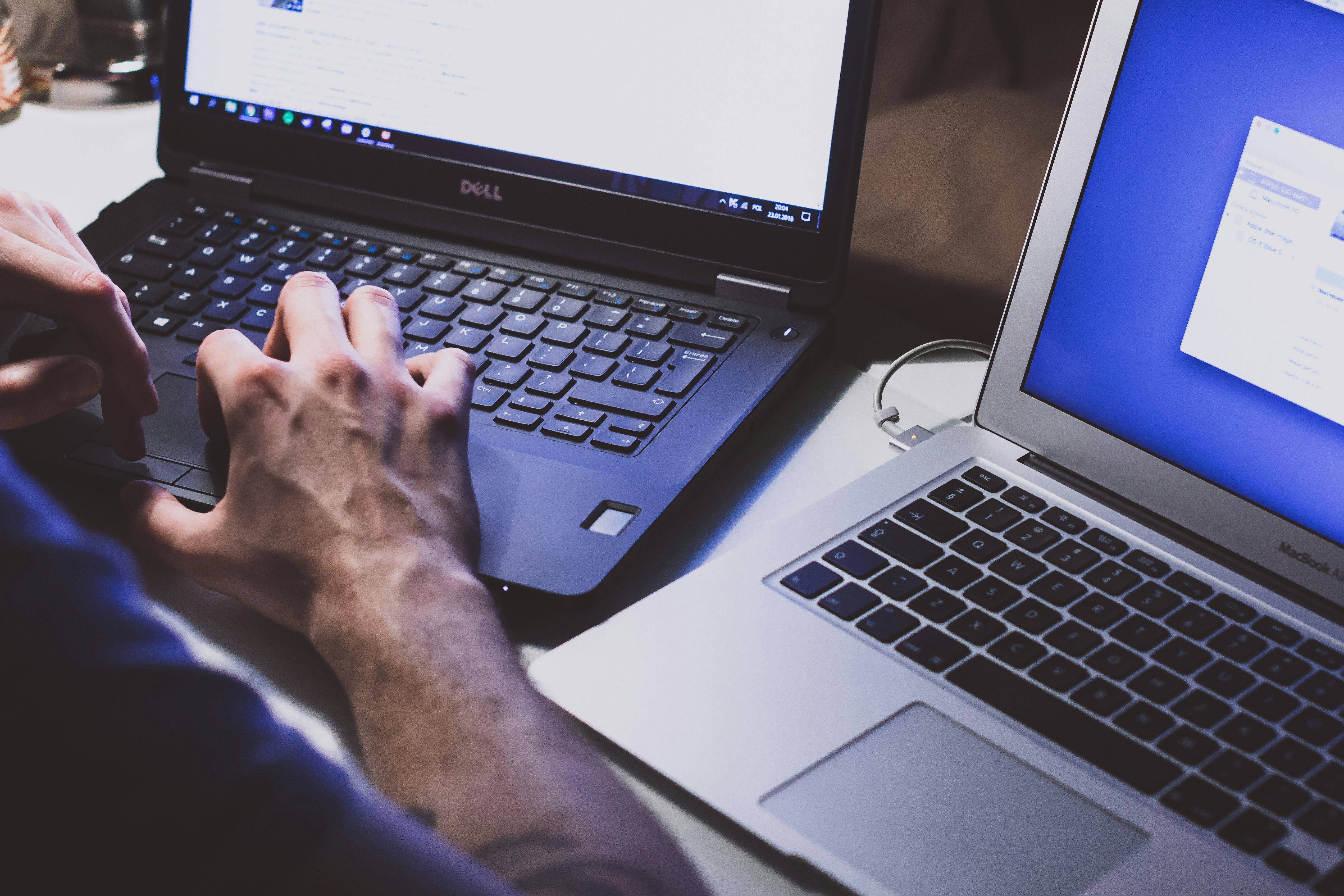 Auf dem Bild sind zwei Laptops zu sehen, einer von Dell und einer von Apple. Eine Hand tippt auf der Tastatur des Dell-Laptops.